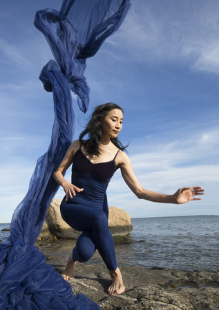 Graceful woman dancer in blue leotard and tights, hurling huge blue fabric into the wind on the beach at Hammonasset State Park in Madison, Connecticut.の写真素材
