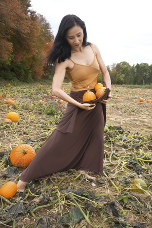 Adult woman dancer dressed in earth tones, standing in a farm field, holding pumpkins in her dress, in Ellington, Connecticut.の写真素材