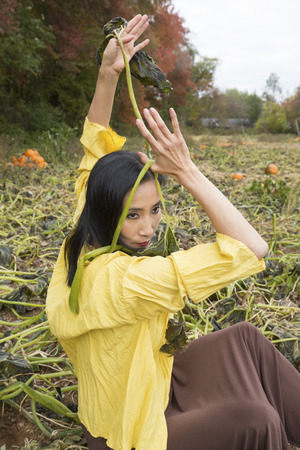 Adult woman dancer, seated in a pumpkin patch, draping vines over her body, on a farm in Ellington, Connecticut.の写真素材