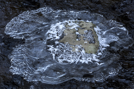 Patterns in an overhanging ice shelf surrounding a rock in Railroad Brook at Valley Falls Park in Vernon, Connecticut in winter.の写真素材