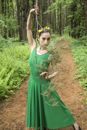 Woman dancing on a path in the woods, in green dress, holding a branch at the Belding Wildlife Management Area in Vernon, Connecticut.の写真素材