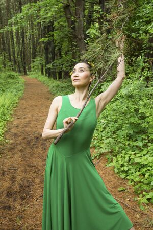 Woman dancing on a path in the woods, in green dress, holding a branch at the Belding Wildlife Management Area in Vernon, Connecticut.の写真素材