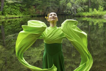 Woman in green dress with long flowing sleeves,dancing on a path in the woods near a pond, at the Belding Wildlife Management Area in Vernon, Connecticut.の写真素材
