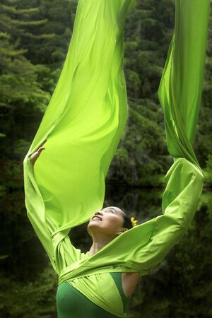 Woman in green dress with long flowing sleeves, dancing on a path in the woods near a pond, at the Belding Wildlife Management Area in Vernon, Connecticut.の写真素材