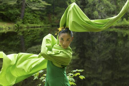 Woman in green dress with long flowing sleeves, dancing on a path in the woods near a pond, at the Belding Wildlife Management Area in Vernon, Connecticut.の写真素材