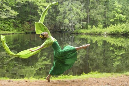 Woman in green dress with long flowing sleeves,dancing on a path in the woods near a pond, at the Belding Wildlife Management Area in Vernon, Connecticut.の写真素材