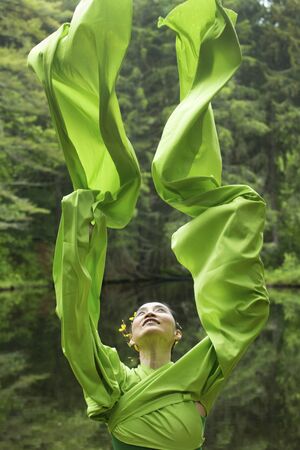 Woman in green dress with long flowing sleeves, dancing on a path in the woods near a pond, at the Belding Wildlife Management Area in Vernon, Connecticut.の写真素材
