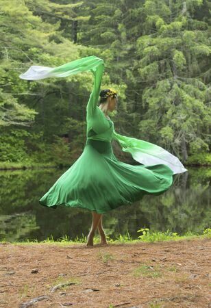 Woman in green dress with long flowing sleeves,dancing on a path in the woods near a pond, at the Belding Wildlife Management Area in Vernon, Connecticut.の写真素材