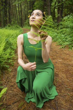Woman dancer in green dress, looking at fern leaves along a path in the woods, at the Belding Wildlife Management Area in Vernon, Connecticut.の写真素材