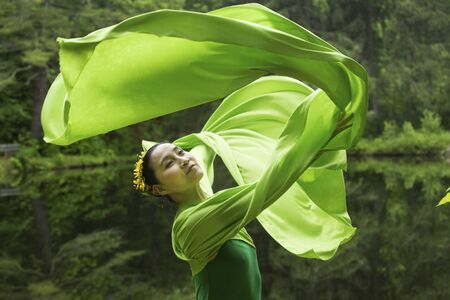 Woman in green dress with long flowing sleeves, dancing on a path in the woods near a pond, at the Belding Wildlife Management Area in Vernon, Connecticut.の写真素材