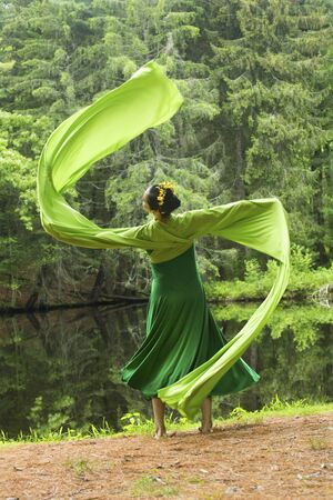 Woman in green dress with long flowing sleeves,dancing on a path in the woods near a pond, at the Belding Wildlife Management Area in Vernon, Connecticut.の写真素材
