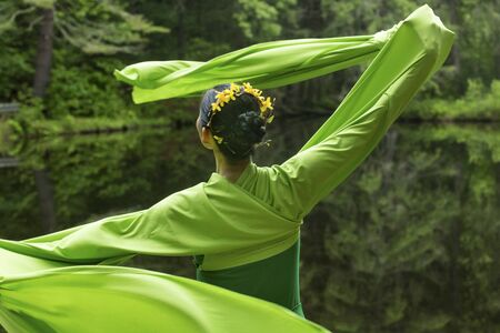 Woman in green dress with long flowing sleeves, dancing on a path in the woods near a pond, at the Belding Wildlife Management Area in Vernon, Connecticut.の写真素材