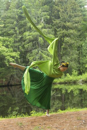 Woman in green dress with long flowing sleeves,dancing on a path in the woods near a pond, at the Belding Wildlife Management Area in Vernon, Connecticut.の写真素材