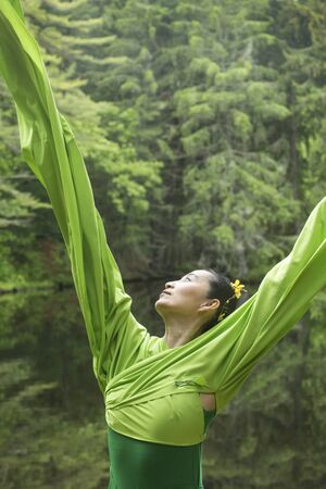 Woman in green dress with long flowing sleeves, dancing on a path in the woods near a pond, at the Belding Wildlife Management Area in Vernon, Connecticut.の写真素材