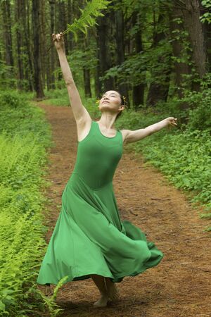 Woman in green dress,  dancing on a path in the woods while holding a fern leaf, at the Belding Wildlife Management Area in Vernon, Connecticut.の写真素材