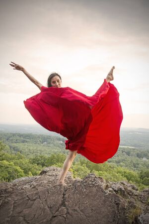Female dancer in flowing red dress, dancing on the rocky summit of the mountain at Penwood State Park in Bloomfield, Connecticut.の写真素材