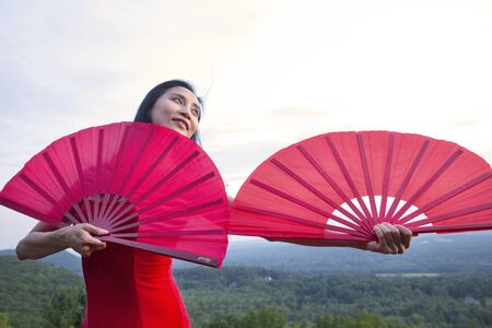 Female dancer in red dress, raising at sunset on the mountain a red fan in each hand, at Penwood State Park in Bloomfield, Connecticut.の写真素材