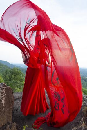 Female dancer in red dress, waving into the wind in late afternoon on the mountain, a red fabric with Chinese calligraphy on it, at Penwood State Park in Bloomfield, Connecticut.の写真素材