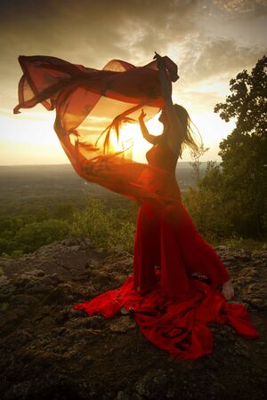 Female dancer in red dress, waving into the wind at sunset on the mountain a red fabric with Chinese calligraphy on it, at Penwood State Park in Bloomfield, Connecticut.の写真素材