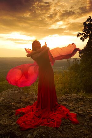 Female dancer in red dress, waving into the wind at sunset on the mountain a red fan with flowing fabric on it, at Penwood State Park in Bloomfield, Connecticut.の写真素材