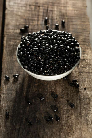 Detail of a lot of black beans in white plate on a wooden table