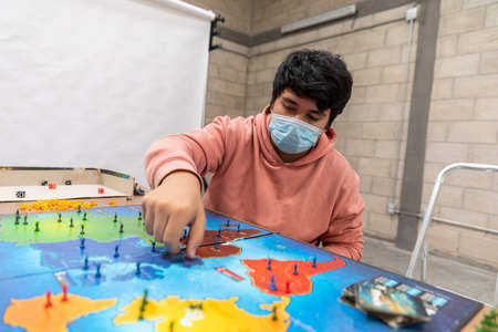 Group of youths with face masks during COVID-19 disease quarantine playing a board game.