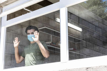 Man in quarantine with face masks looking out of their house through the window.
