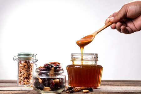 Honey dripping from the honey dipper into a glass jar. Close up. Healthy organic coarse honey...