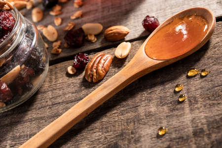 Honey dripping into a glass jar. Close up. Healthy oatmeal and granola over a wooden tableの写真素材