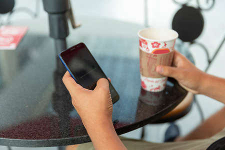 Smiling and handsome young man drinking coffee in the mall with his cellphone