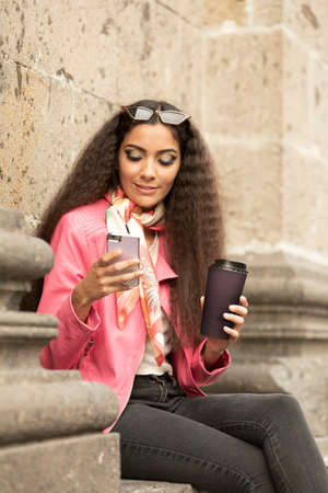 Beautiful latin woman with sunglasses, smiling happy with her cellphone in outdoor parkの写真素材
