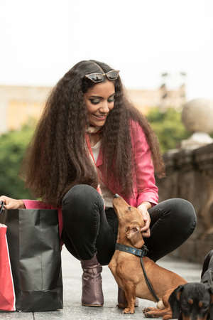 Beautiful young woman wearing fashionable clothes walking on the street with tender dogsの写真素材