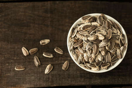 Texture detail of a lot of girasol seeds with peel in a deep dish over a wooden tableの写真素材