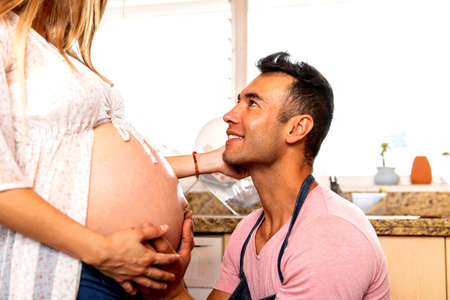 Amorous father with his pregnant woman in the kitchen of his home .. Husband with apron working