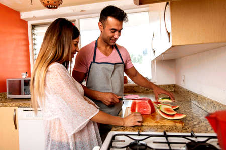 Amorous father with his pregnant woman in the kitchen of his home .. Husband with apron workingの写真素材