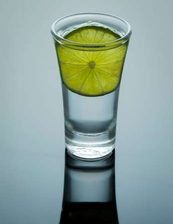Shot of tequila with salt and lemon and reflection on bright table.の写真素材