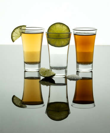 Shot of tequila with salt and lemon and reflection on bright table.