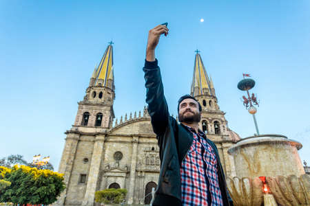 Young tourist taking a selfie with his cell phone in the Cathedral in the city of Guadalajara, Jalisco, Mexico.の写真素材