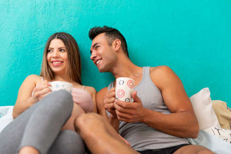 Pregnant woman.Young real couple of happy married in the bedroom of their house enjoying a cup of coffee.の写真素材