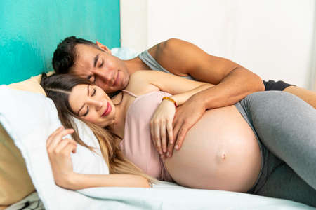 Young real couple of happy married in the bedroom of their house. Pregnant woman.の写真素材