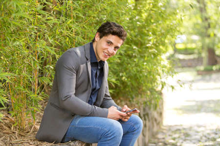 Front view portrait of a young businessman smiling walking towards camera and texting on phoneの写真素材