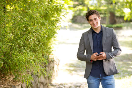 Front view portrait of a young businessman smiling walking towards camera and texting on phone