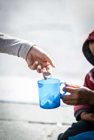 Detail of woman's hand giving a coin to a homeless person, and sad boy in the background.