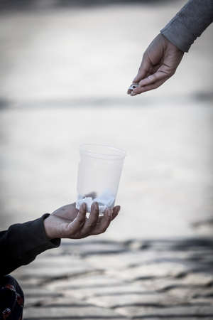 Detail of woman's hand giving a coins to a homeless personの写真素材