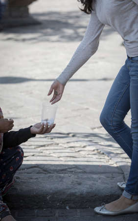 Detail of woman's hand giving a coin to a homeless person, and sad boy in the background.