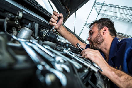 Mechanic hand checking and fixing a broken car in car service garage