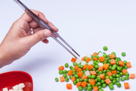 Hand with forceps moving peas and carrotsの写真素材