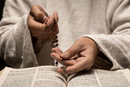 Jesus Christ praying to God with the Holy Bible and the Holy Rosary in the hands in the dark black nightの写真素材
