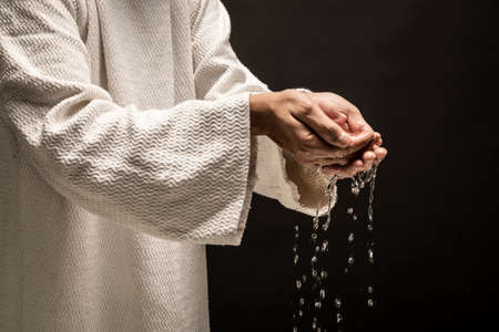 Water for Baptism pouring out of the hands of Jesus Christ during a dark night.の写真素材