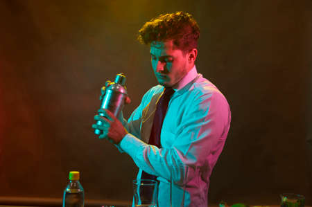Barman preparing alcoholic drink with a cocktail shaker at the bar with some glasses of liqueur.の写真素材